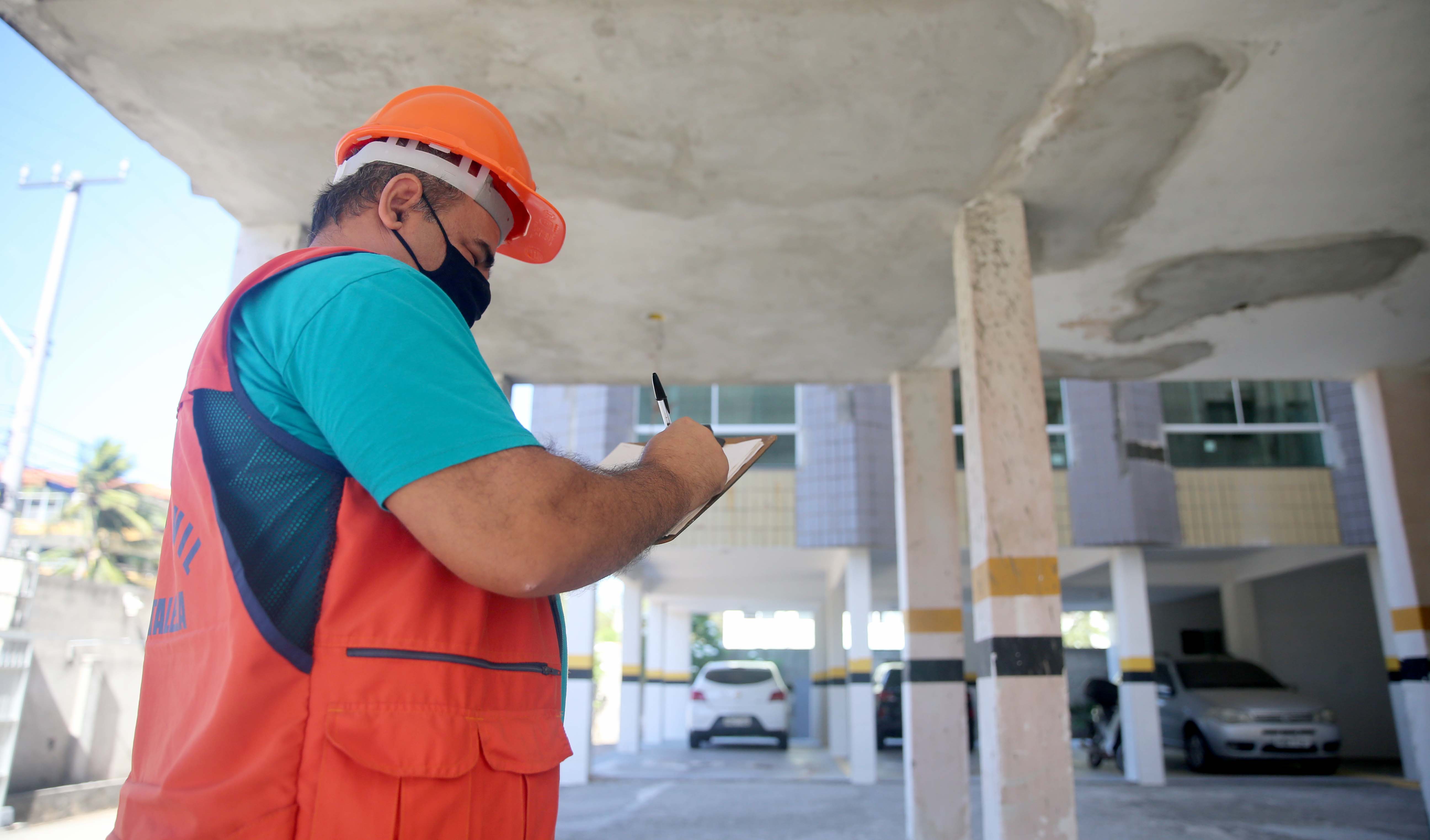 um técnico da Defesa Civil avalia a área de garagem de um prédio. No teto da garagem, as marcas de cimento indicam que foram feitos reparos